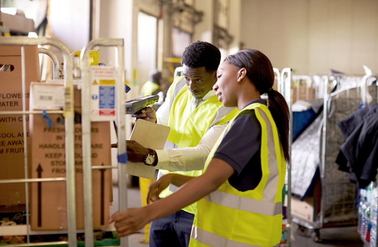 Woman prepares roll cage for delivery, checked by supervisor